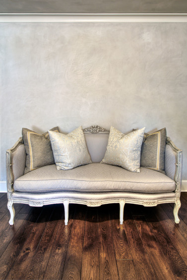 Serving as a perfect backdrop to the luscious silk covered settee, the plaster was toned to complement, creating an elegant and soothing master retreat. Sources: Margaux silk in pewter on bench and topiary scroll fabric in ice on pillows from Beacon Hill. Plaster by Segreto.