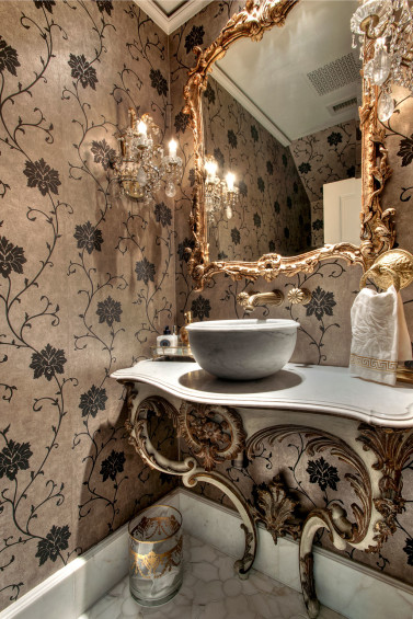 In the formal powder room a shimmery wallcovering provides an unexpected departure from the tone of the rest of this house. Sources: Wallcovering from Kravet, Inc. Sink from Chateau Domingue. French crystal sconces from MAI.