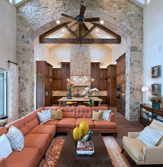 The family room, designed by Sharon Staley and divided from the kitchen only by the 18-foot stone archway, reflects a rustic ambiance found in elegant Italian country homes. The exposed wooden trestle beams and the stone columns provide perfect contrast for the tailored sectional sofa and clean lines of the cocktail table.