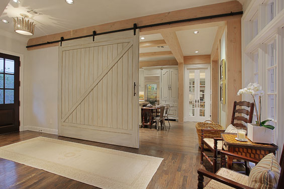 The barn door, which lends character and charm to this entry feature, was actually a new door that Leslie from Segreto Finishes refinished to look aged. The door also serves as a divider between the kitchen and more formal social areas when the couple entertains. All the beams were stained in a pine aged finish.