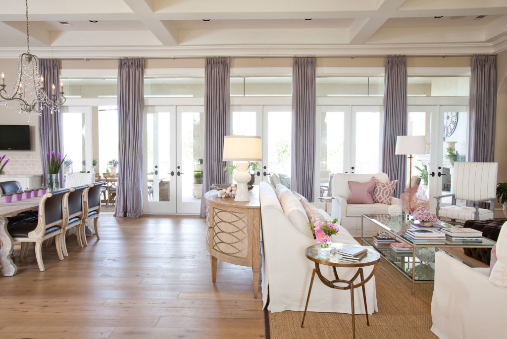 In the open living room, a wall of windows spans the space allowing filtered light as well as a great view of the outdoors. Custom furniture upholstered in white linen; sofa table from Neirmann Weeks; custom drapery in S Harris Fabricut fabric, Topaz. Soft blushy pink and grey blue pillows add soft color.
