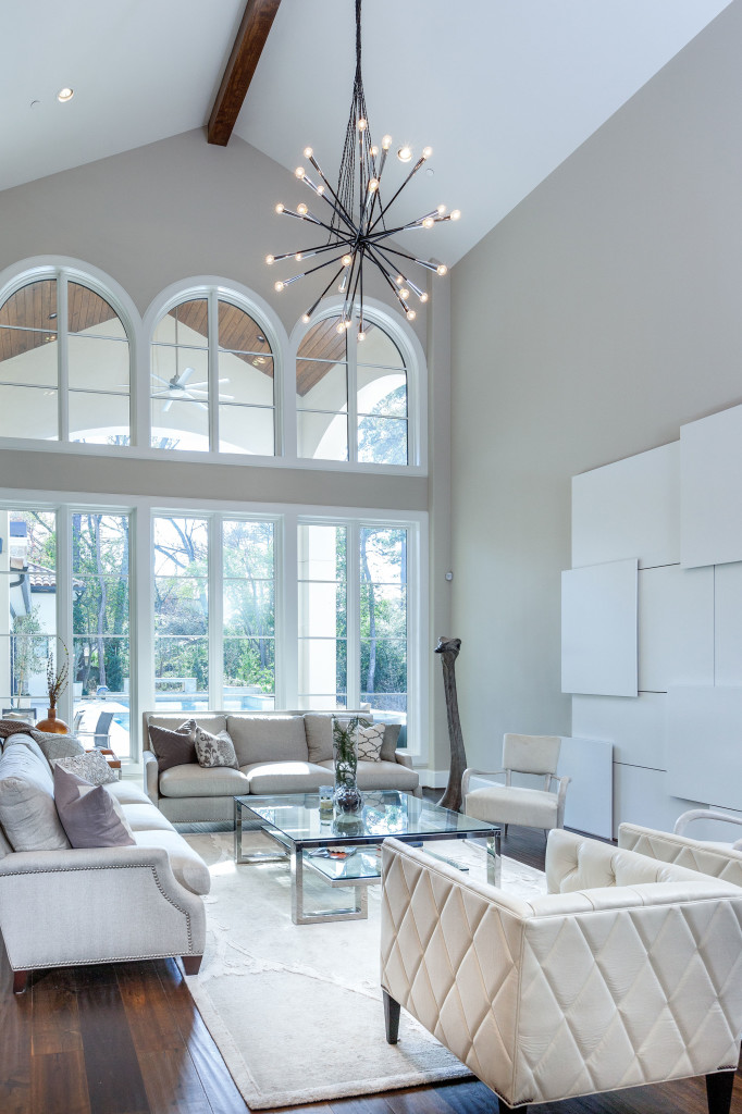The contemporary aesthetic and monochromatic color scheme of the art and furniture in this living room juxtapose beautifully with the wall of arched windows and lush, verdant backyard scene