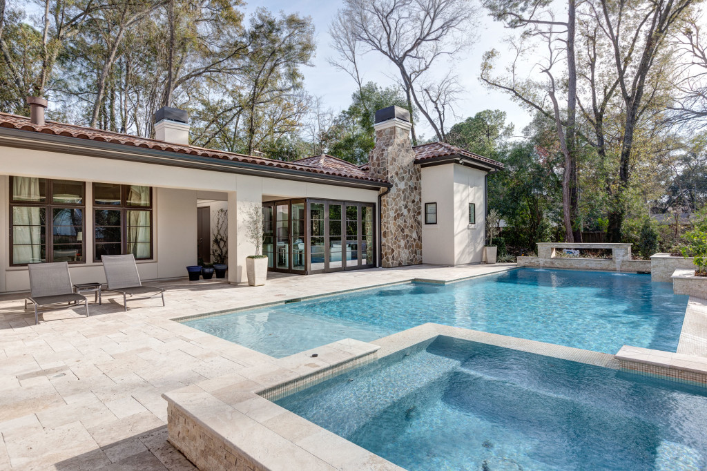 This view of the outdoor living space includes the hot tub and the swimming pool with a tanning ledge. The far end of the pool features a fire element and the guest casita — a fully equipped living/dining space has glass walls that open on two sides.
