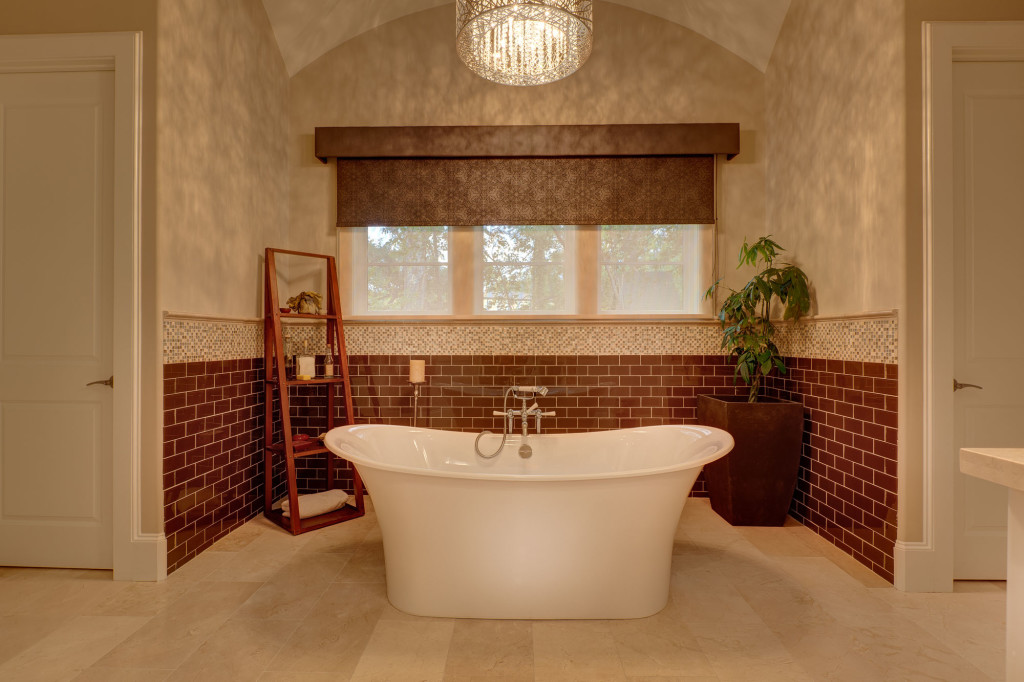 The stark white soaking tub is accentuated by the smooth marble floor, the brick subway tiles, the pebble effect of the accent tile and the texture of the faux finish on the wall. Natural light along with the elegant chandelier bring a warm ambiance to bath time.
