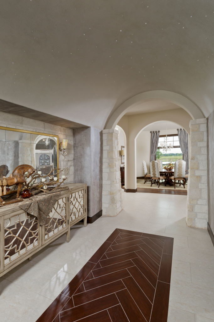 In the foyer, fiber optic Texas “stars” by Starfield Design twinkle from the barrel-shaped ceiling overhead, softly lighting the custom-painted ceiling details by A Creative Design. The polished porcelain plank flooring features a custom wood insert.