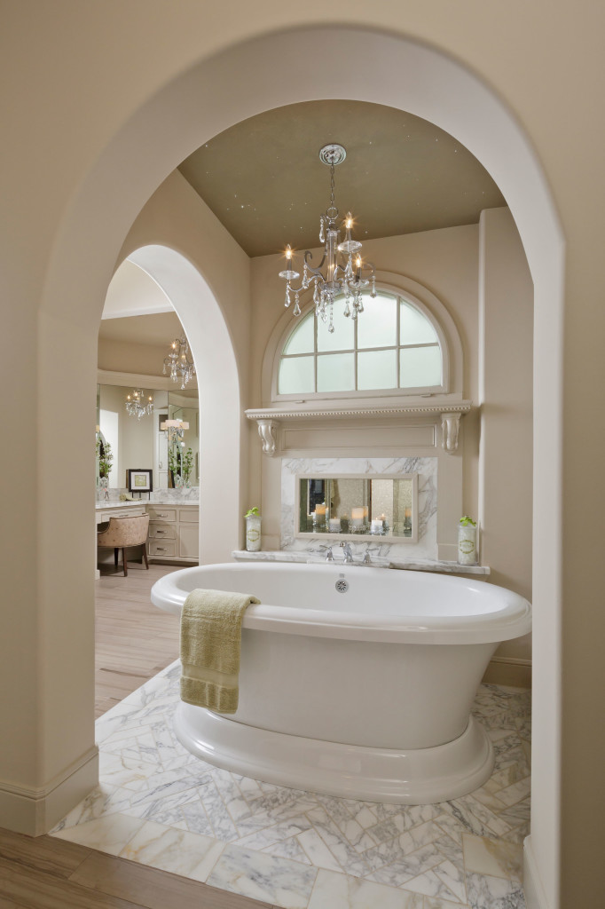 The master bath features a graceful oval-shaped air tub by Aquatic, placed atop real Calacatta marble laid in a herringbone pattern. Above – natural daylight filters in through a Velux “sun tunnel.” And at night, you’ll have your own personal stars overhead thanks to the built-in fiber optics. And for a touch of whimsical romance, above the tub is a niche with an antique distressed mirror that reflects a candle detail. In the far left background, her separate dressing area is a glamorous personal space, with custom vanity and cabinets designed to keep everything in its perfect place.