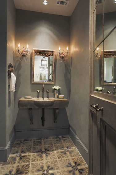 The formal powder room is a small jewel. Reclaimed pine door was fitted with antique mirror and opens up to even more repurposed elements found at Chateau Domingue. The painted concrete tile floors and blue limestone sink are taken straight from the French countryside and define the charming atmosphere the homeowner and designer were trying to achieve.