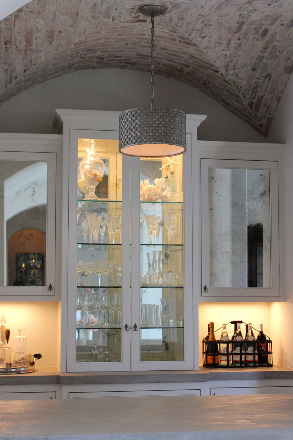An antique mirror backsplash frames the bar area while the brick barrel vault ceiling is the crowning feature. The area is accessorized beautifully with a contemporary drum light fixture.