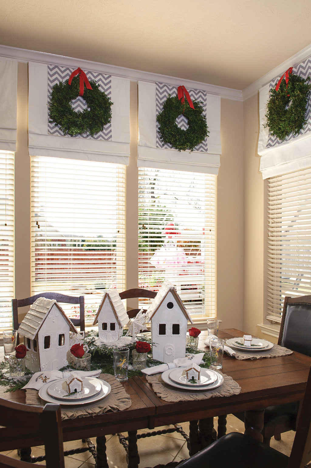 Fresh Boxwood wreaths and gray chevron fabric are the perfect backdrop for the gingerbread houses and Christmas china in the breakfast room. Handmade Gingerbread houses with monogrammed individual smaller houses were created for each place setting and family member.