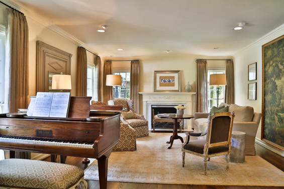 A stunning Carol Piper rug lies underfoot in the formal living room. Custom upholstered chairs mingle with a vintage French chair upholstered in gray mohair velvet. The French cartoon wall hanging (right) is from Twenty Six Twenty. Custom linen drapes are an exquisite touch. The piano left by the previous owners is a delightful addition. “We are having fun with it,” says the homeowner.