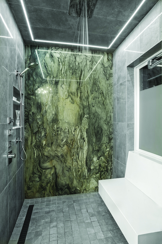 Blue fusion granite on the back wall of the walk-in shower defines the luxury in the master bath. The granite is lit by a recessed LED light channel from Edge Lighting. Both the lighting and the Zuchetti rain head are integrated into the tile. A floating bench is wrapped in white quartz.