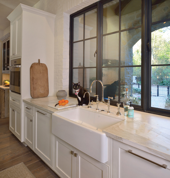 The family cat, Tux, has found a place of honor near the oversized farmhouse sink. Calcutta marble countertops with plumbing and hardware from Hollywood hardware.