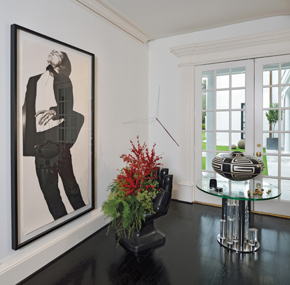 In the back entry hall, a holiday arrangement is creatively displayed in a vintage hand chair found in New Orleans. The vintage lucite and chrome table is a find from a trip to Palm Springs. Art by Robert Longo.
